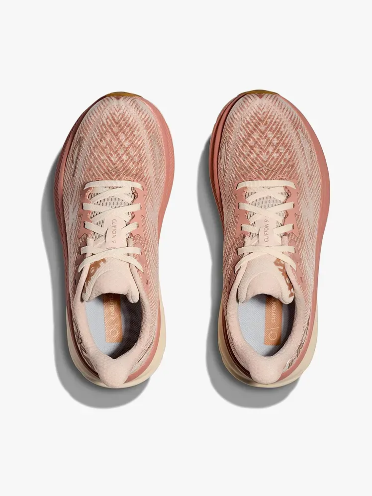 Sepatu kets Clifton 9 dengan warna ungu muda lembut dan karang bermerek dengan latar belakang abu-abu muda