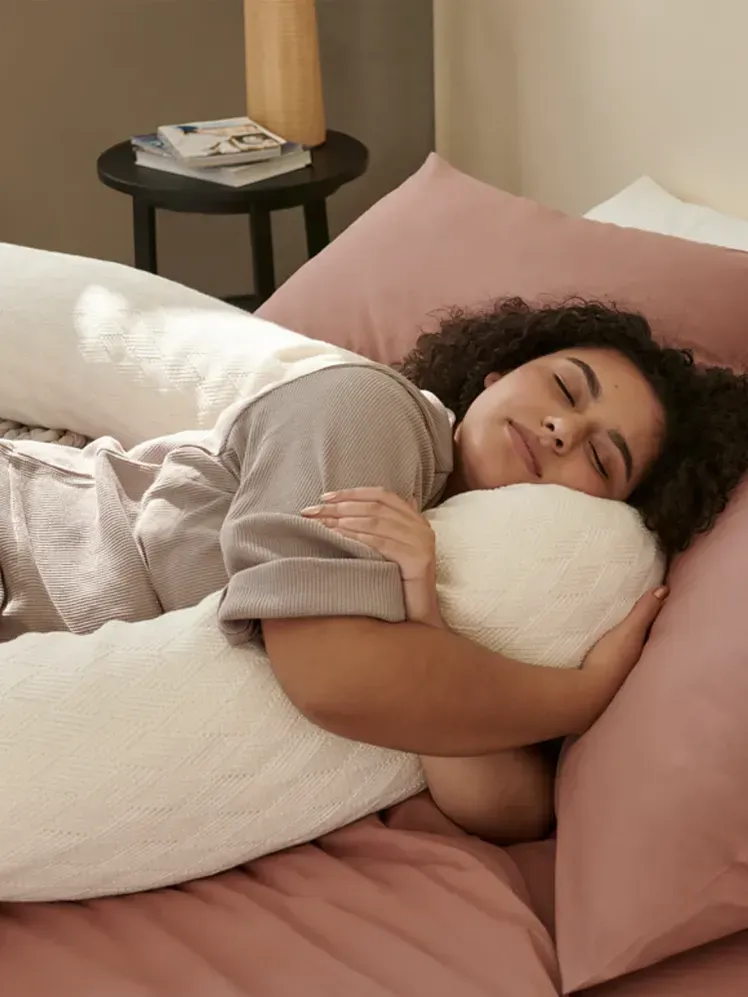 Подушка білого кольору, яку модель тримає на ліжку