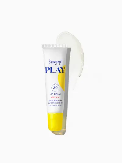 Supergoop! Spill Lip Balm SPF 30 i merket hvit og gul tube på toppen av produktprøven på lysegrå bakgrunn