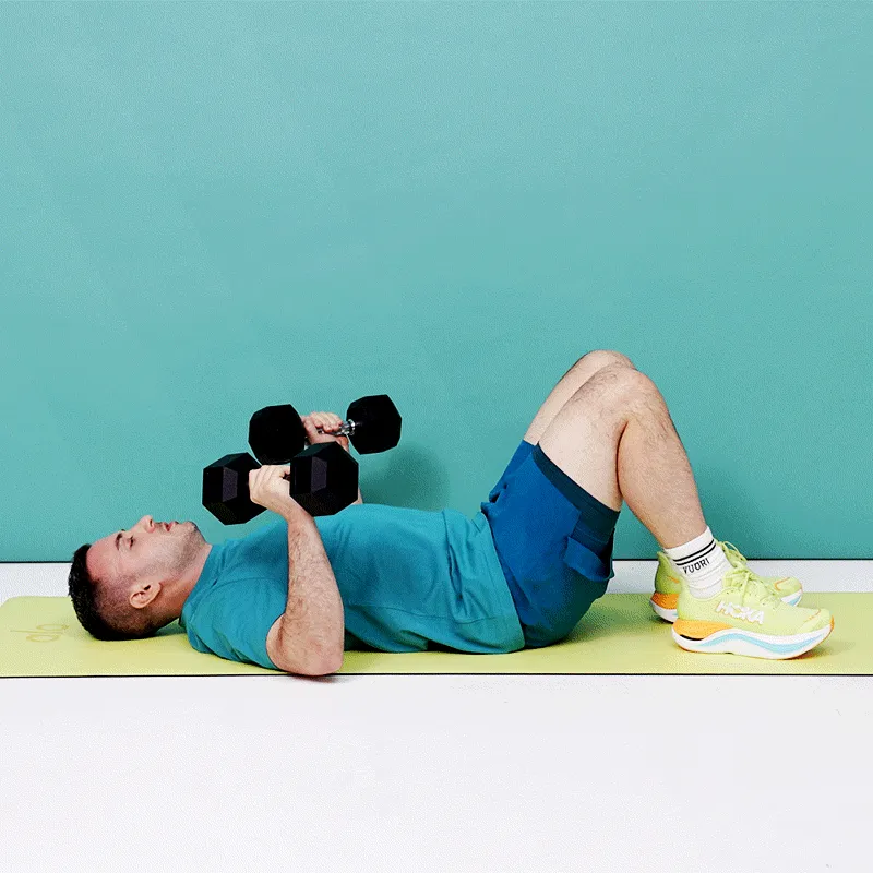 Ляжте обличчям догори, зігніть коліна, а стопи поставте на підлогу. Тримайте легкі гантелі в кожній руці долонями до...