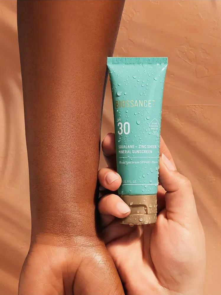 Squalane + Zinc Sheer Mineral fényvédő SPF 30, amelyet a modell karokkal körülvéve tart