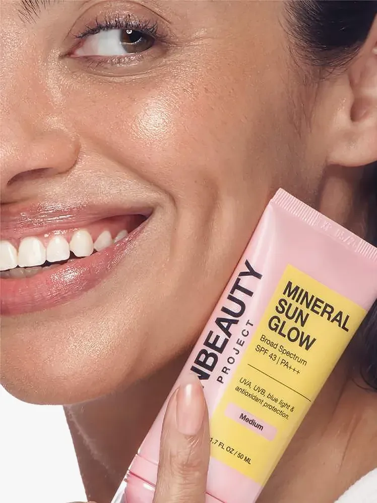 Mineral Sun Glow fényvédő márkás tubusban, amelyet mosolygós modell tart