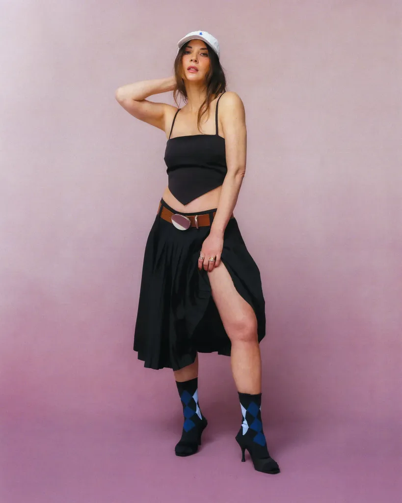 Slika lahko vsebuje Olivia Munn Oblačila Krilo Dodatki Pas Odrasla oseba Klobuk Obutev Čevelj Obleka Obraz in glava