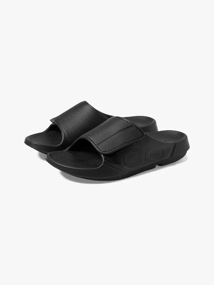 Oofos Ooahh Sport Flex Slide z markowego materiału na jasnoszarym tle