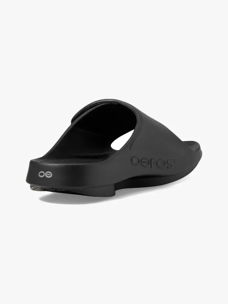 Oofos Ooahh Sport Flex Slide z markowego materiału na jasnoszarym tle