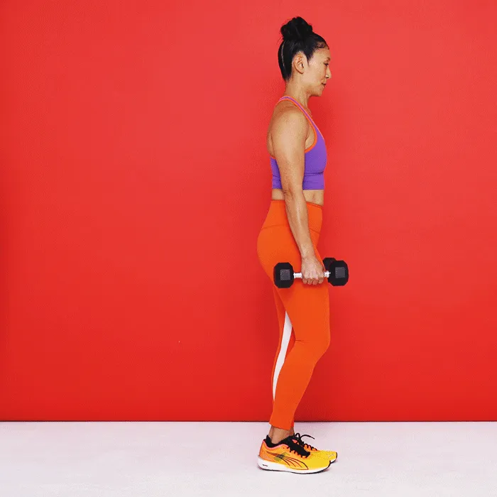 Tenez-vous debout, les pieds joints, en tenant un haltère dans chaque main devant vos jambes. C