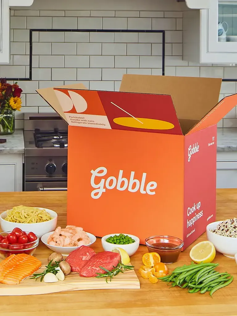 रसोई काउंटर टॉप पर विभिन्न खाद्य पदार्थों के बगल में ब्रांडेड नारंगी और लाल डिब्बे में भोजन सेवा