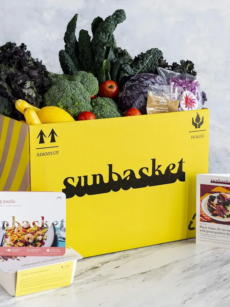 रेसिपी कार्डों से घिरा सामग्री से भरा सनबास्केट ब्रांडेड सब्सक्रिप्शन बॉक्स