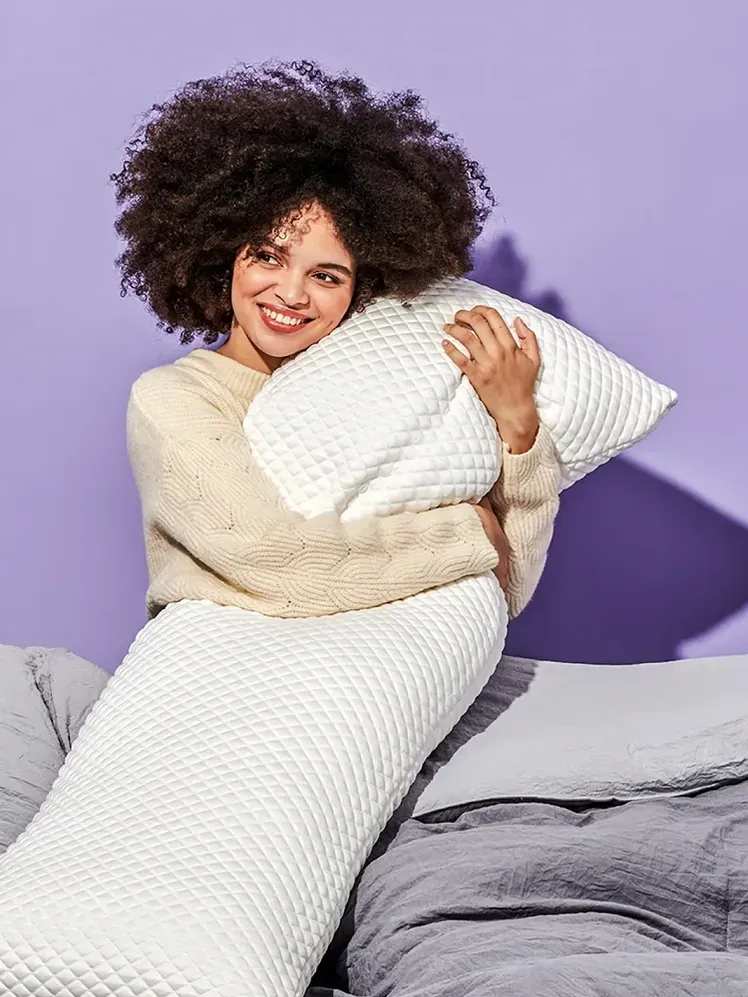 Puff Body Pillow en blanco sostenido por el modelo en la cama en una habitación violeta