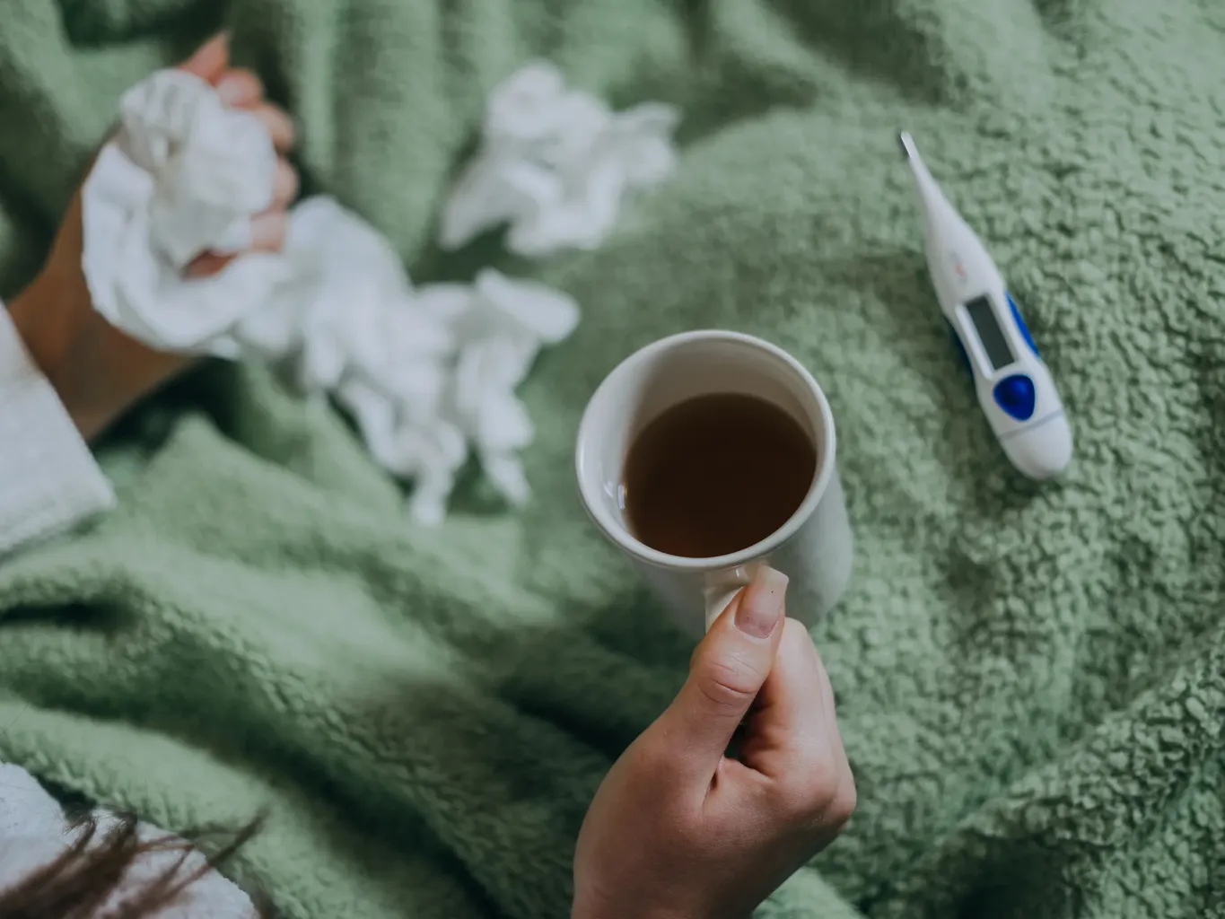 yeşil bir battaniyenin üzerinde elinde termometre ve mendil tutan bir kadının elleri