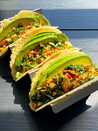 ਇੱਕ ਟੈਕੋ ਹੋਲਡਰ ਵਿੱਚ ਤਿੰਨ ਐਵੋਕਾਡੋ ਅਤੇ ਟੋਫੂ ਨਾਸ਼ਤਾ ਟੈਕੋ