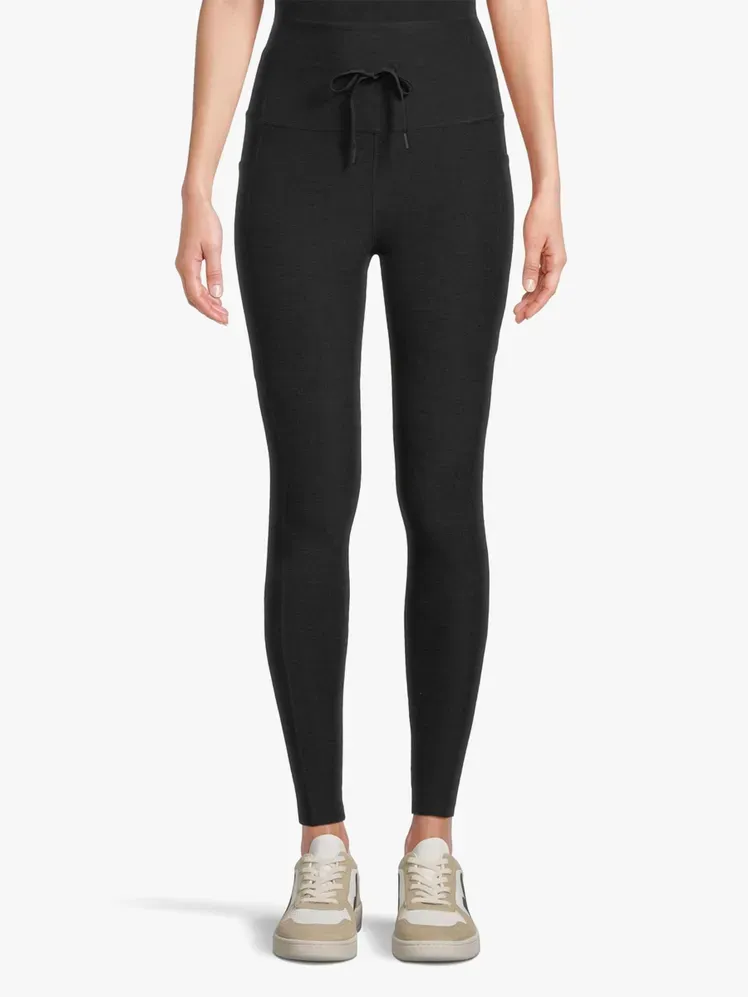 हल्के भूरे रंग की पृष्ठभूमि पर मॉडल पर गहरे भूरे रंग में स्पेसडाई गो पॉकेट मिडी लेगिंग