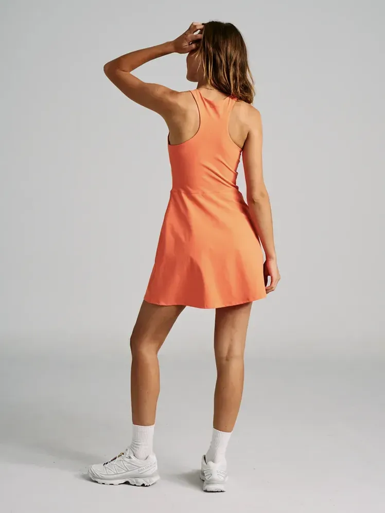 Gaun Voli dengan warna oranye lembut pada model dengan latar belakang abu-abu