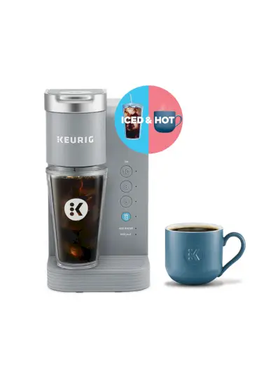 K-Iced Essentials Iced and Hot Single-Serve K-Cup Pod-Kaffeemaschine in silberner Farbe neben einer gedämpften blauen Tasse auf weißem Hintergrund
